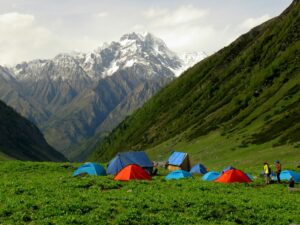 tente bleue et rouge sur un champ d'herbe verte près d'une montagne enneigée pendant la journée