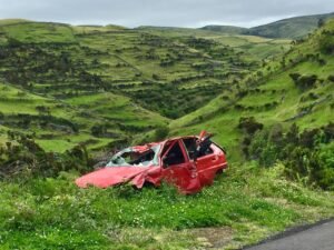 Une voiture rouge accidentée est abandonnée dans une vallée verdoyante et pittoresque, mettant en évidence le déclin rural.