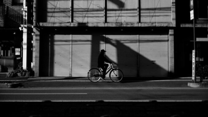 La silhouette d'un homme faisant du vélo devant un bâtiment dans la rue de la ville.