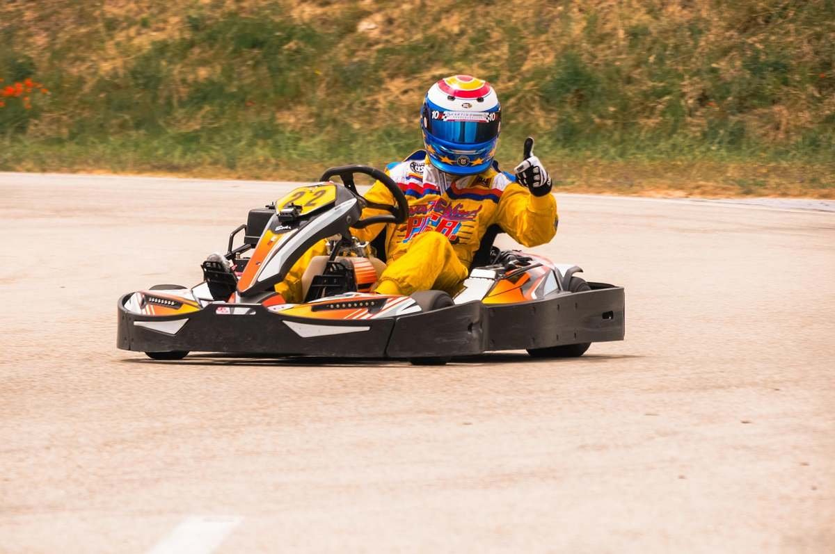 Pilote en combinaison jaune et casque bleu conduisant un kart jaune sur piste asphaltée Pilote en combinaison jaune et casque bleu conduisant un kart jaune sur piste asphaltée