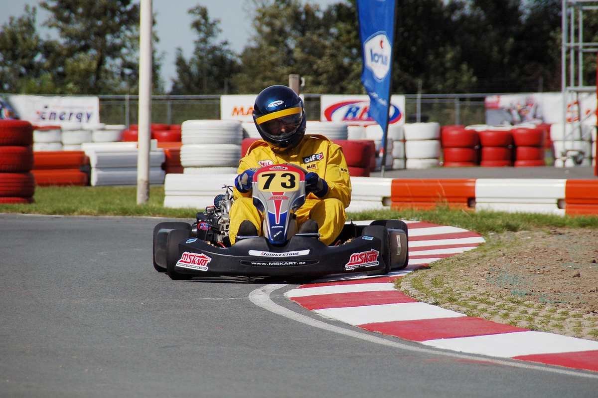 Kart jaune et bleu numéroté 79 négociant un virage sur circuit avec barrières blanches et rouges Kart jaune et bleu numéroté 79 négociant un virage sur circuit avec barrières blanches et rouges