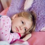 Fillette en pyjama à motifs repose sur lit rose avec peluche violette