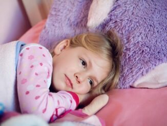Fillette en pyjama à motifs repose sur lit rose avec peluche violette