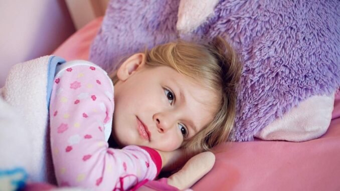 Fillette en pyjama à motifs repose sur lit rose avec peluche violette
