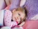 Fillette en pyjama à motifs repose sur lit rose avec peluche violette