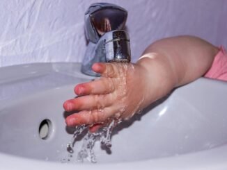 Petite main d'enfant en rose se lavant sous un robinet dans un lavabo blanc