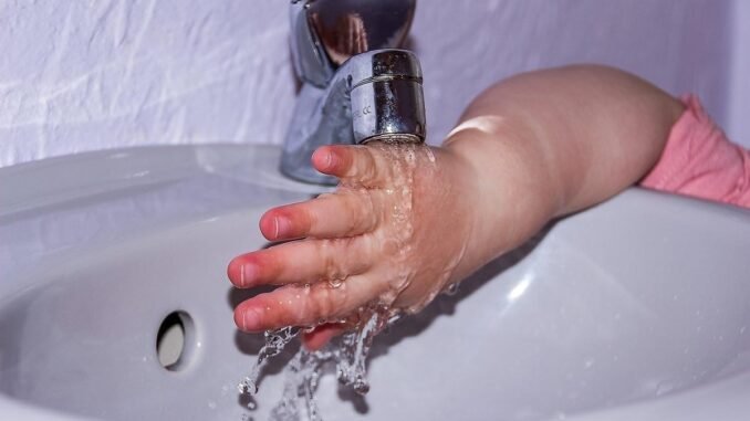 Petite main d'enfant en rose se lavant sous un robinet dans un lavabo blanc