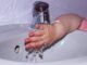Petite main d'enfant en rose se lavant sous un robinet dans un lavabo blanc