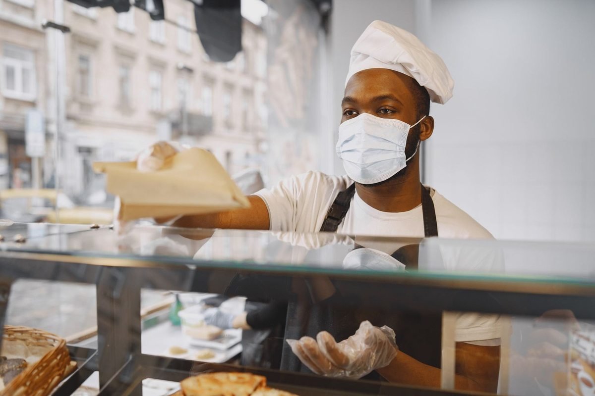 Homme en tenue de cuisiner distribue des plats à travers une vitrine de vente