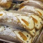 Des cannoli garnis de crème, zestes d'orange et raisins, saupoudrés de sucre