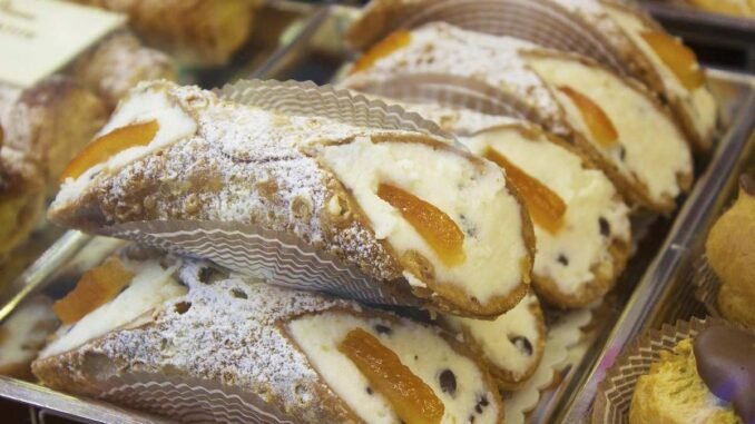 Des cannoli garnis de crème, zestes d'orange et raisins, saupoudrés de sucre